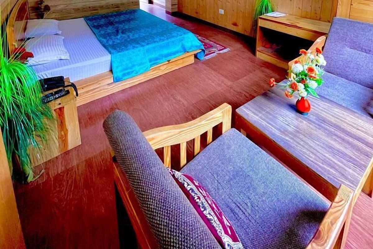 A compact room with a bed, a sofa, a small table, a TV, and a ceiling fan.