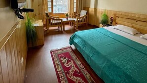 A hotel room with a bed, a ceiling fan, a TV mounted on the wall, a dining table with chairs, and a window with curtains. - Amar Villa Manali (Manali)