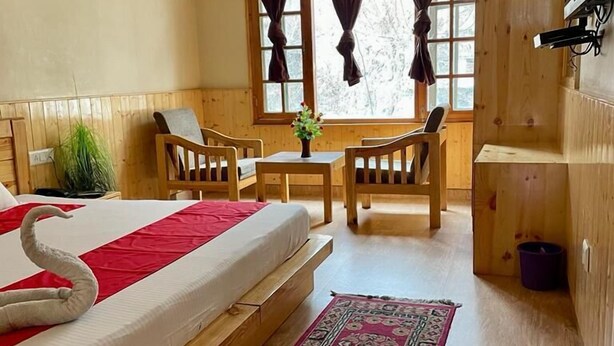 A wooden room with a bed, a small table, two chairs, a TV, and a window with curtains. - Amar Villa Manali (Manali)