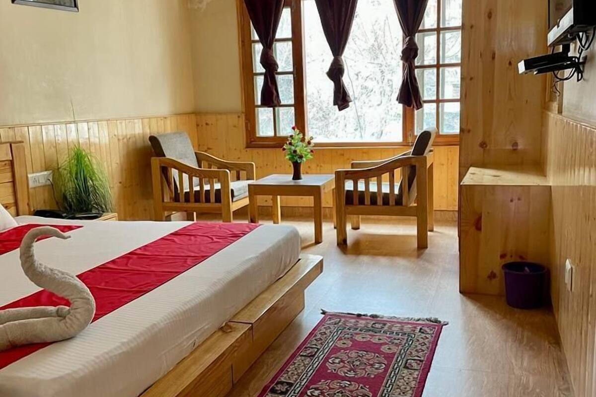 A wooden room with a bed, a small table, two chairs, a TV, and a window with curtains.