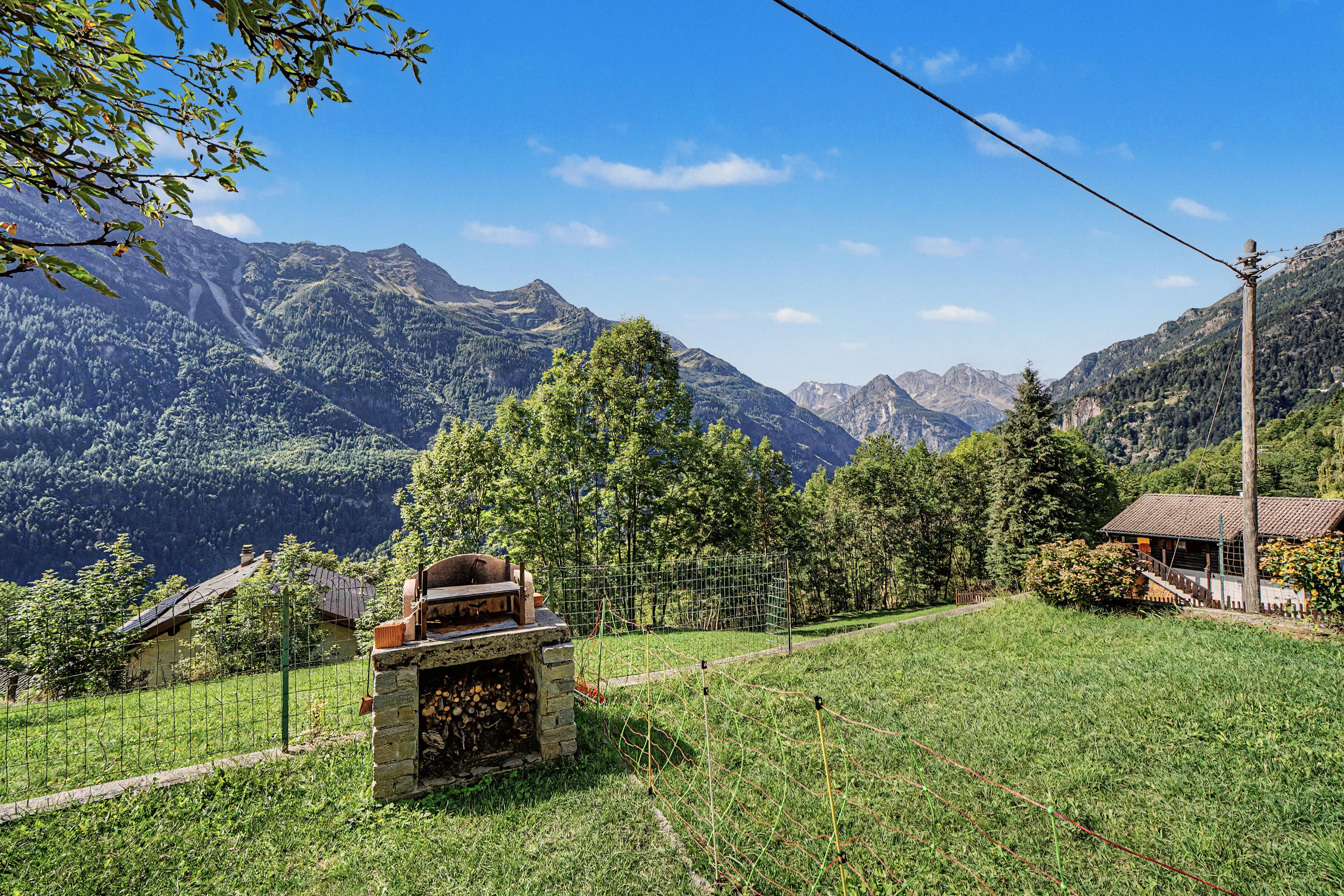 Eine ländliche Berglandschaft mit einem Steinofen, einem Holzhaus und wolkenlosem Himmel.