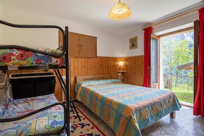 Habitación con literas, una cama individual, paneles de madera, una ventana con cortinas rojas y vista a la vegetación.