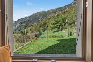 Vista per la finestra d'un paisatge de muntanyes amb un jardí tancat per una tanca.