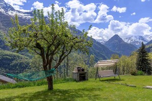 Un hamac, un barbecue et un espace de détente abrité, le tout installé dans un champ verdoyant avec des montagnes en arrière-plan.