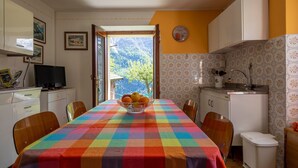Una cocina con una mesa de comedor, sillas, un bol de fruta, un lavamanos y una ventana con vistas a la montaña.