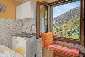 Une cuisine compacte équipée d’un évier et de placards, une fenêtre donnant sur un paysage montagneux, et un banc agrémenté d’un coussin.