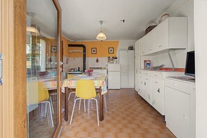 Une cuisine compacte avec un coin repas, dotée d’un sol carrelé, d’un réfrigérateur et d’une table avec des chaises.