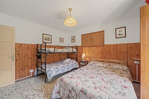 Une chambre avec des lits superposés, une armoire en bois, une table de chevet avec une lampe et des tableaux encadrés accrochés au mur.