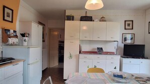 Eine kleine Küche mit Essbereich, einem Kühlschrank, einer Mikrowelle und einem Fernseher.