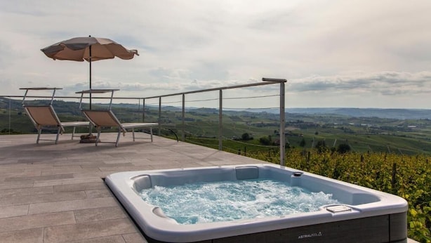 A hot tub on a terrace with chairs and an umbrella, overlooking a vineyard. - Casa SOLE, swimming pool and wellness (Castiglione Tinella)