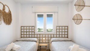 Una habitación con dos camas, una mesita, una ventana con vistas y una lámpara fijada a la pared.
