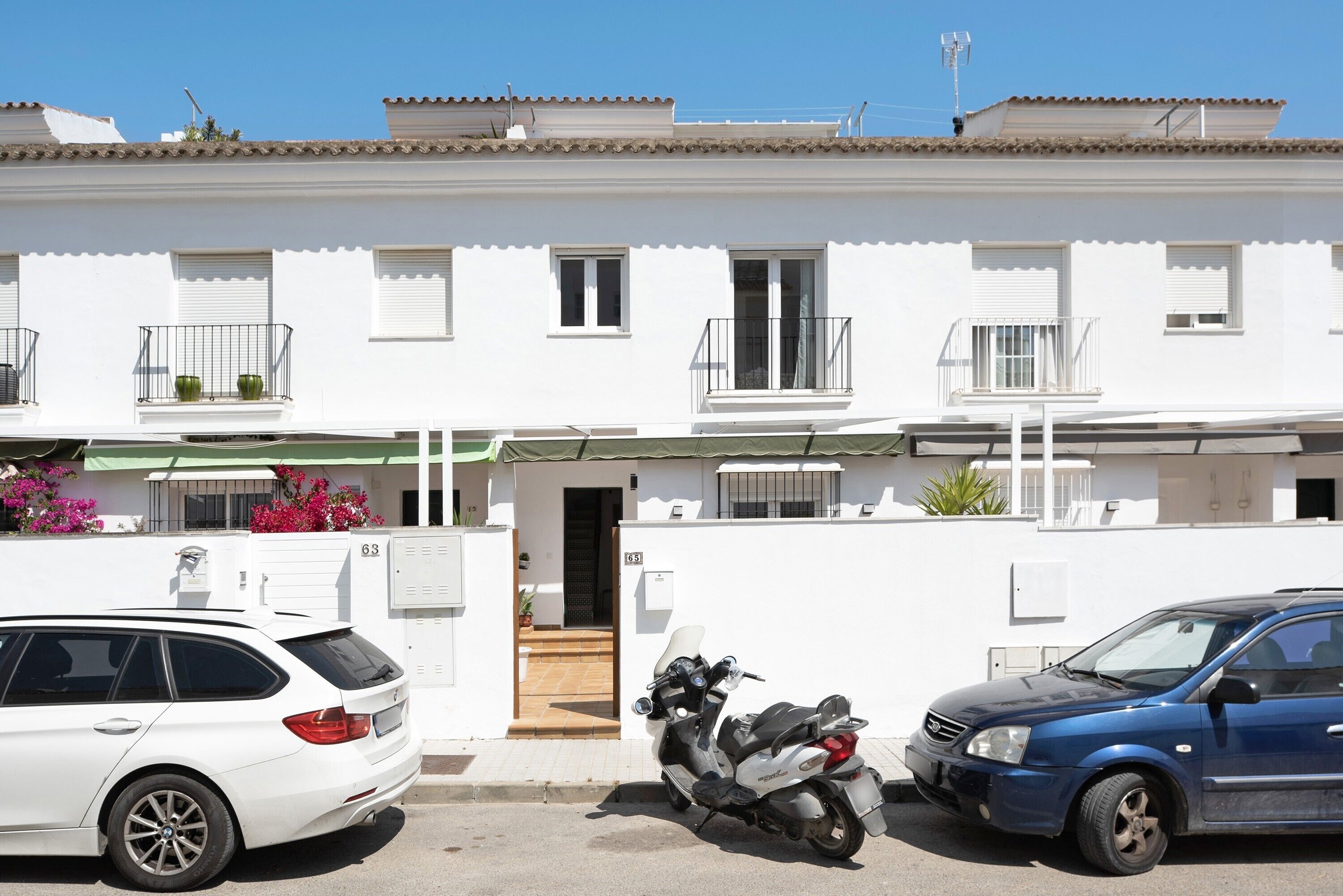A white building with balconies, a white car, and a blue car parked in front.
