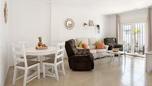 Una sala de estar con una mesa de comedor blanca, sillas, un sofá y un sillón reclinable.