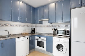 A kitchen with blue cabinets, a Bosch refrigerator, a microwave, a dishwasher, and a washing machine.