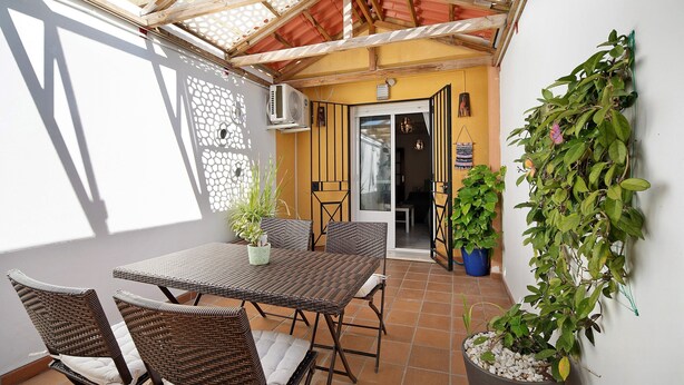 Un patio con una mesa, sillas, una planta en maceta y una puerta que da a un espacio interior.