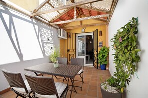 Een terras met een tafel, stoelen, een plant in pot en een deur naar een binnenruimte.