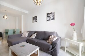 Una sala de estar moderna con un sofá gris, una mesa de centro blanca y una mesita auxiliar de vidrio con un jarrón.