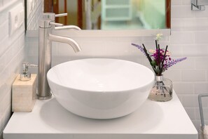 Een witte wastafel met een grote wasbak, een chromen kraan en een kleine vaas met paarse bloemen.