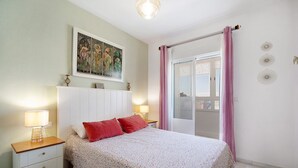 Un dormitorio con cama, mesita de noche, lámpara, una obra de arte y vistas al exterior por una ventana.