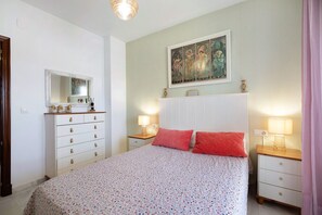 Een slaapkamer met een bed, een kaptafel, een nachtkastje, een spiegel en een schilderij aan de muur.