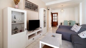 Una sala moderna con un televisor de pantalla plana, un mueble de TV blanco, un sofá gris y una pequeña mesa.