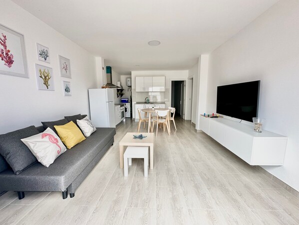 A modern living room with a grey sofa, a small coffee table, and a TV on a white stand.
