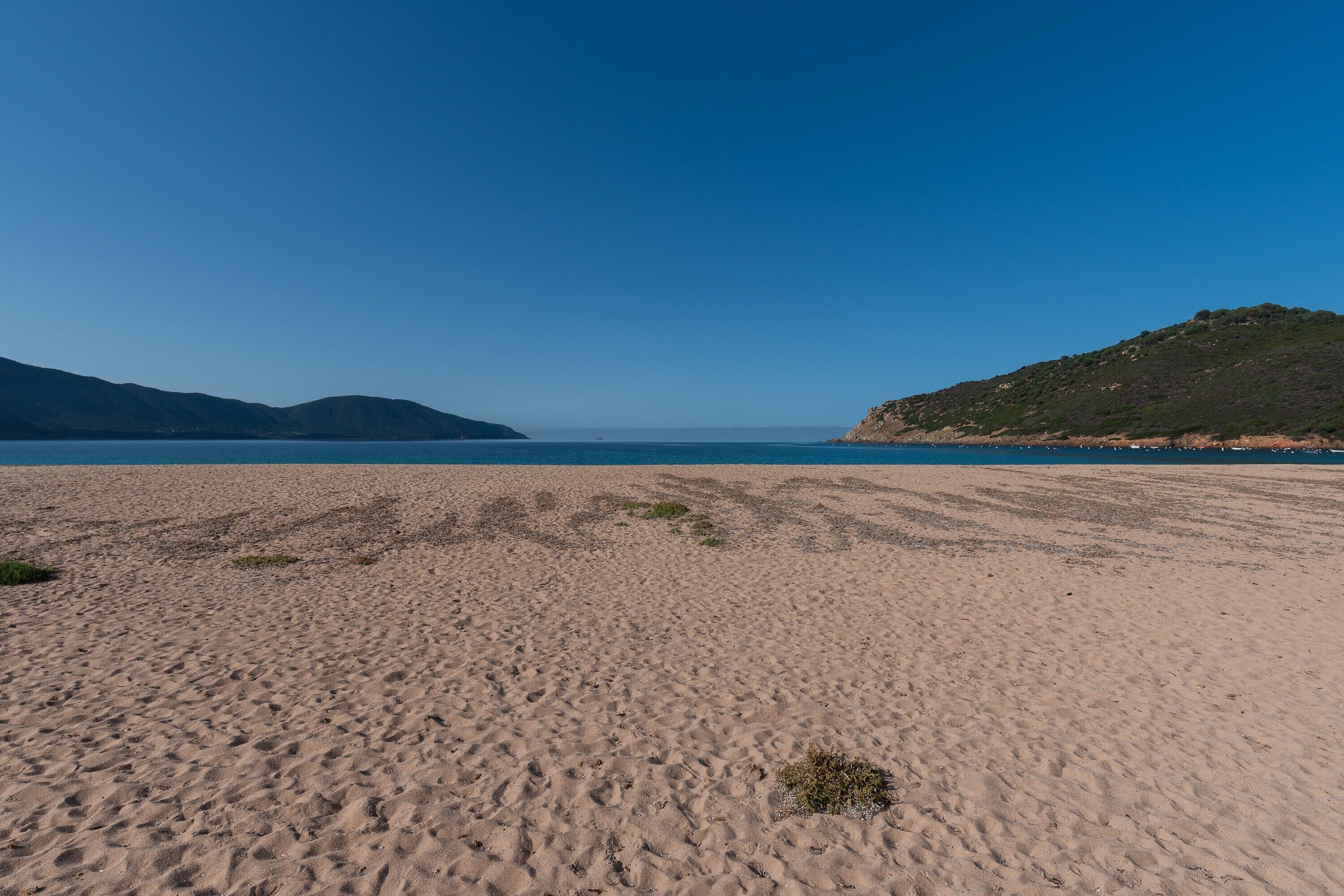 A beach with sand, a clear sky, and distant hills.