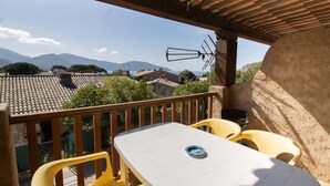Un balcón con mesa y sillas, vista a casas y montañas, además de una pérgola de madera.