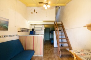 A compact kitchen with a wooden counter, a blue sofa, a ladder, and a staircase leading to an upper level.