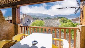 A balcony with a table and chairs, overlooking a village with houses and mountains.