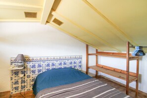 A small, single-bed room with a sloped ceiling, a wooden bunk bed, a bedside lamp, and a tiled wall with a decorative pattern.