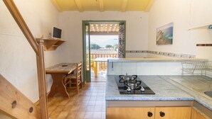 A kitchen with a gas stove, wooden cabinets, a dining table with chairs, and a view through an open door.