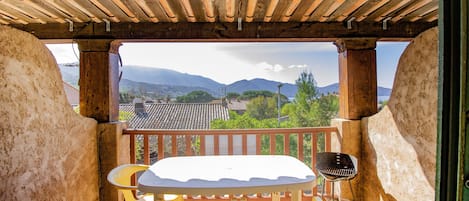 A balcony with a wooden pergola, a table, chairs, and a grill.