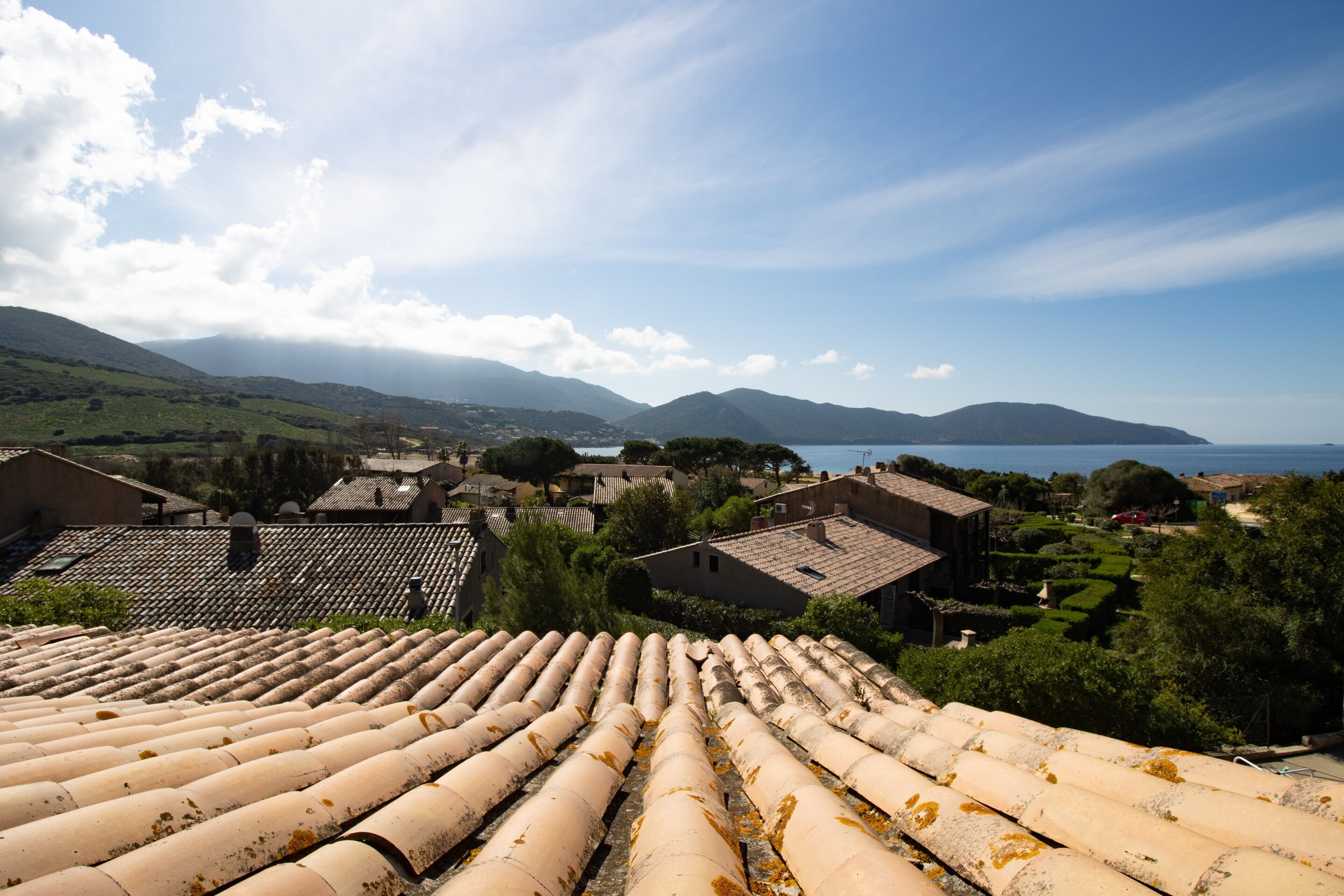 A coastal village with terracotta rooftops, traditional buildings, and a view of the sea and mountains.