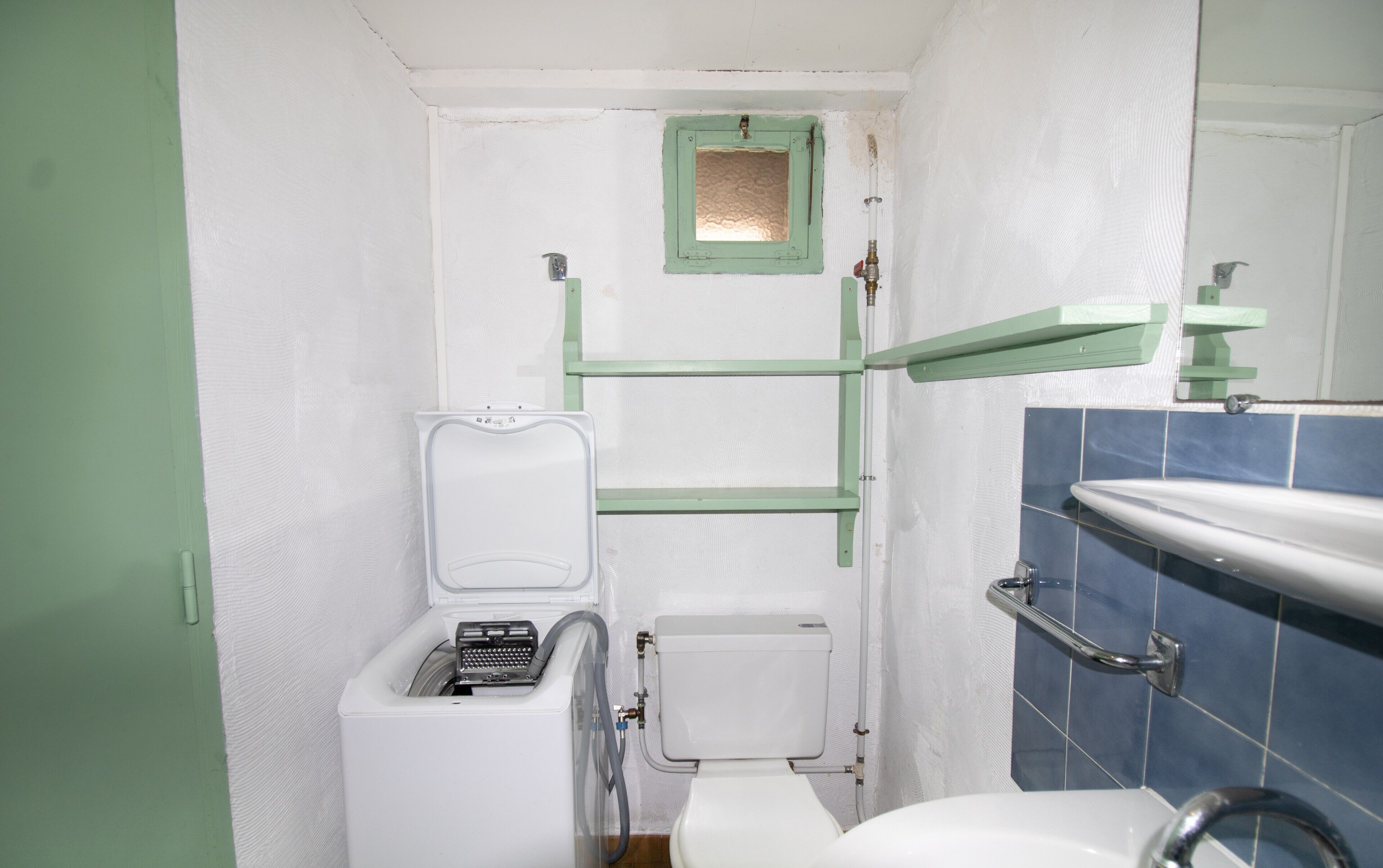 Een kleine badkamer met toilet, wastafel, spiegel en een groen plankje.