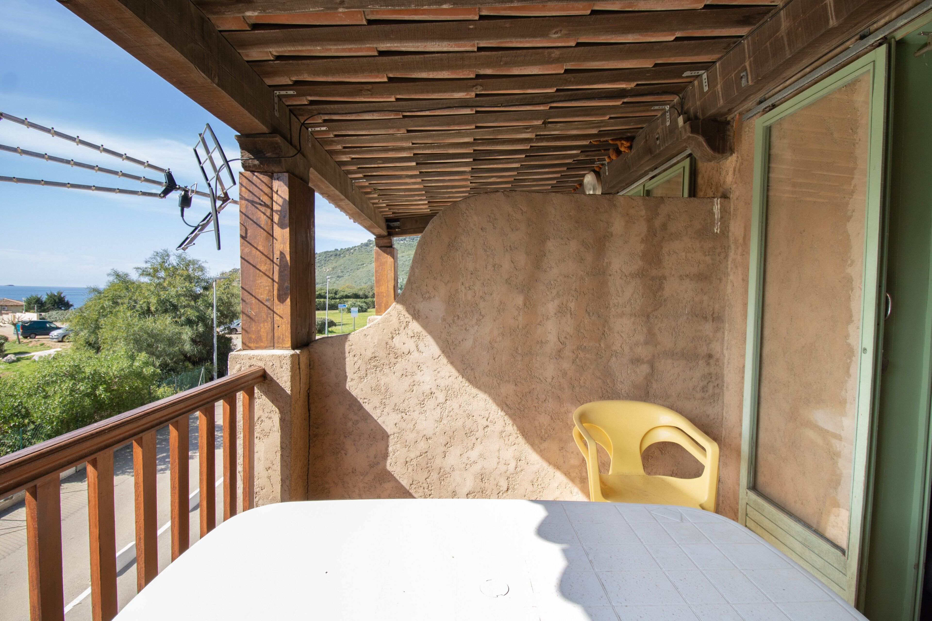 Een balkon met een houten hekwerk, een gele stoel en uitzicht op het landschap.