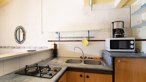 A kitchen with a gas stove, sink, microwave, and a hanging pot holder. - "Le Quattru" Apartment with Sea View, Wi-Fi, and Air Conditioning (Appietto)