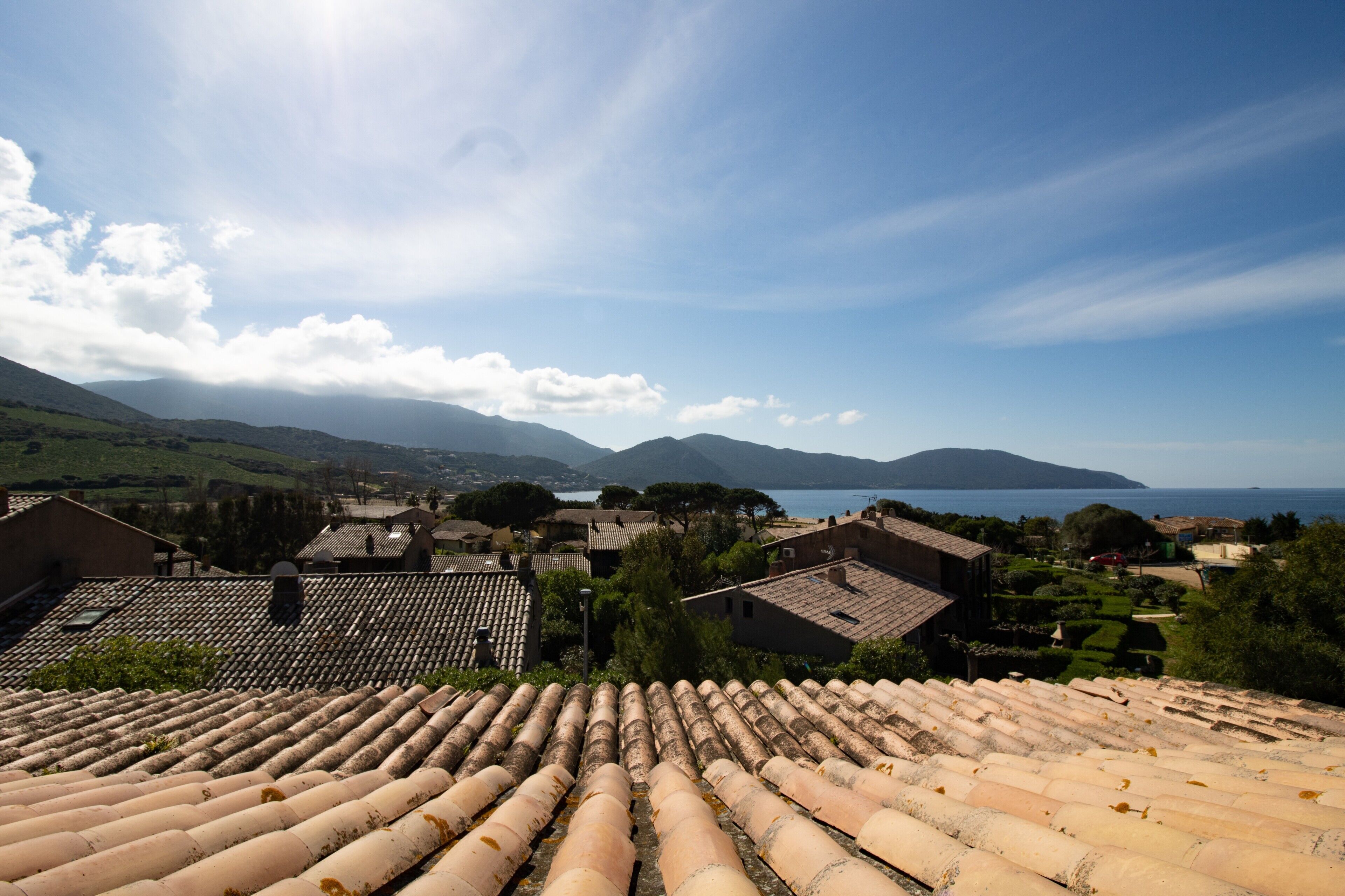 Un village côtier aux toits de tuiles rouges, sous un ciel dégagé, offrant une vue sur la mer.