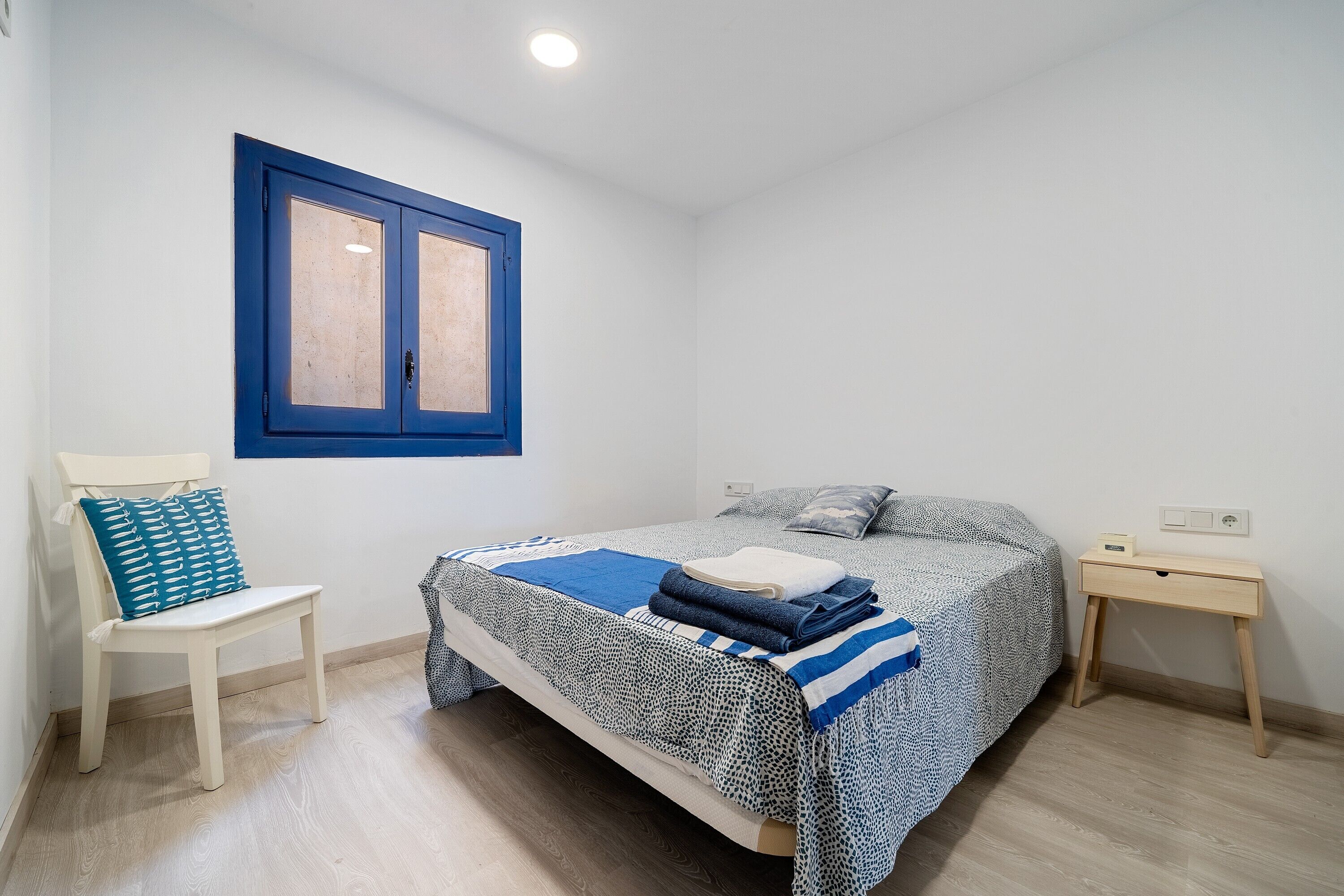 A bedroom with a bed, a chair, a desk, and a window.