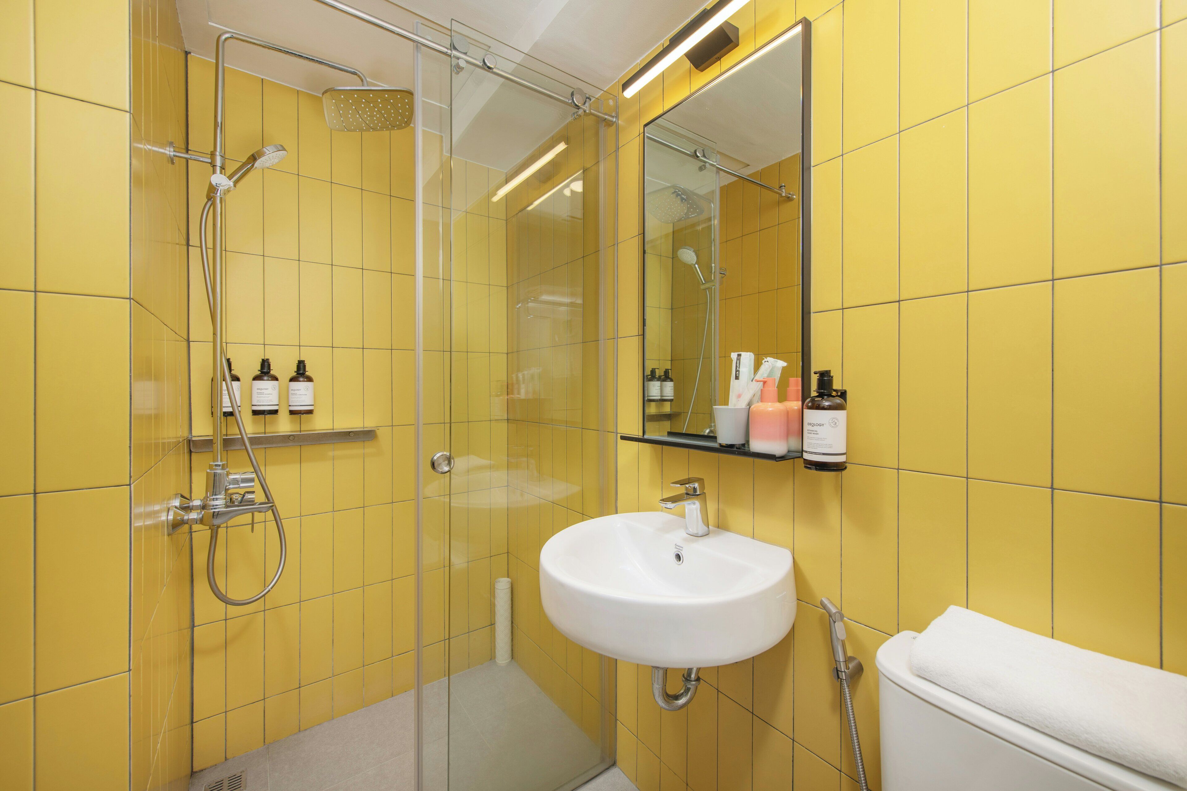 Un baño con azulejos amarillos, una cabina de ducha de vidrio, un lavabo blanco y un espejo.
