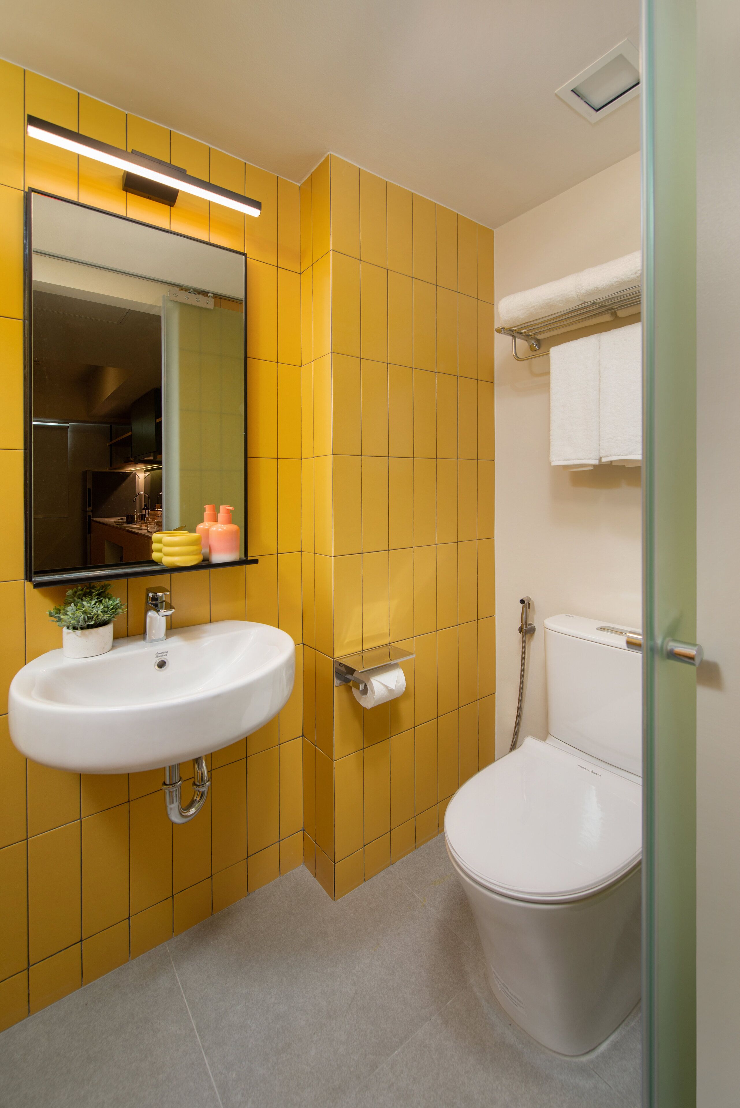 A bathroom with yellow tiled walls, a white sink with a mirror above it, a toilet, and a glass shower enclosure.