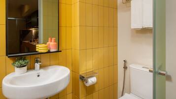 A bathroom with yellow tiled walls, a white sink with a mirror above it, a toilet, and a glass shower enclosure.