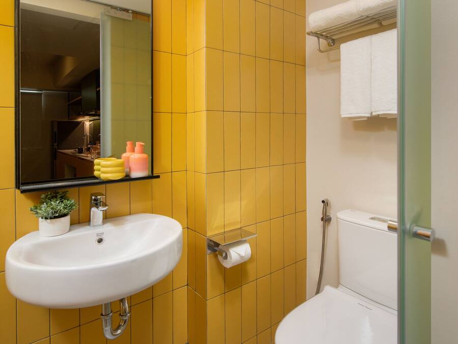 A bathroom with yellow tiled walls, a white sink with a mirror above it, a toilet, and a glass shower enclosure.