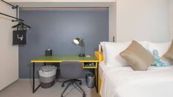 Quarto com uma cama, escrivaninha com cadeira, luminária, cesta e lixeira.