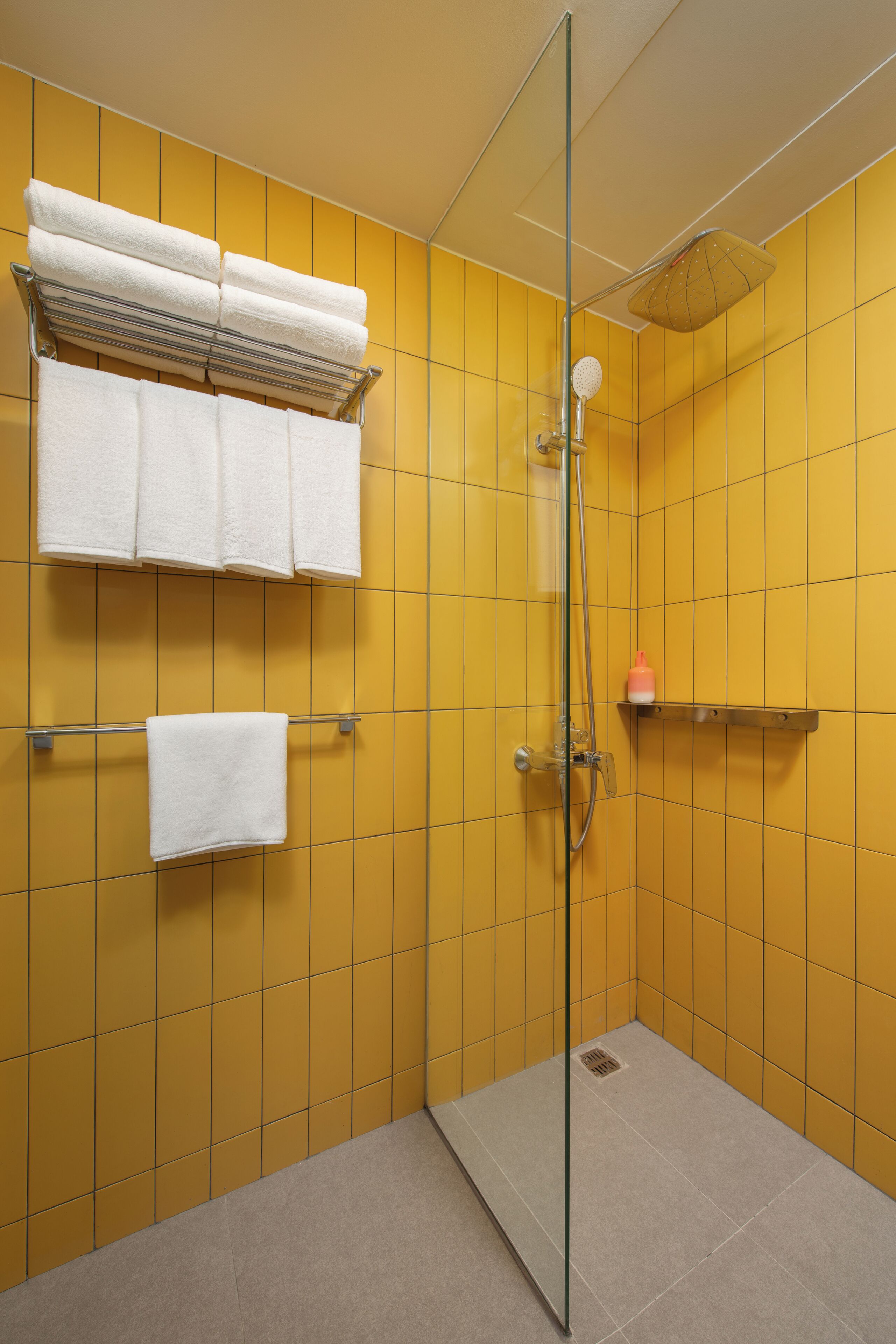 Un baño con paredes de azulejos amarillos, cabina de ducha de cristal y toallas blancas sobre barras de metal.