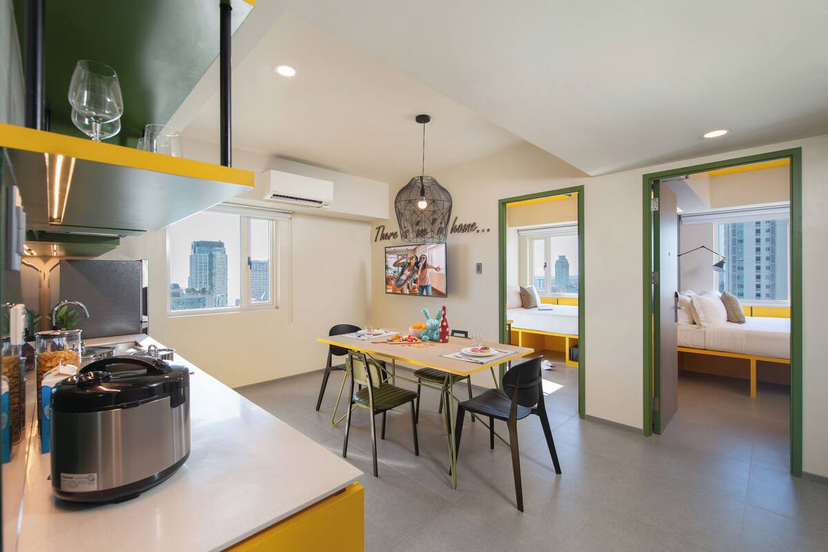 Cozinha moderna com fogão embutido, área de refeições com cadeiras e mesa, e vista da cidade através de grandes janelas.