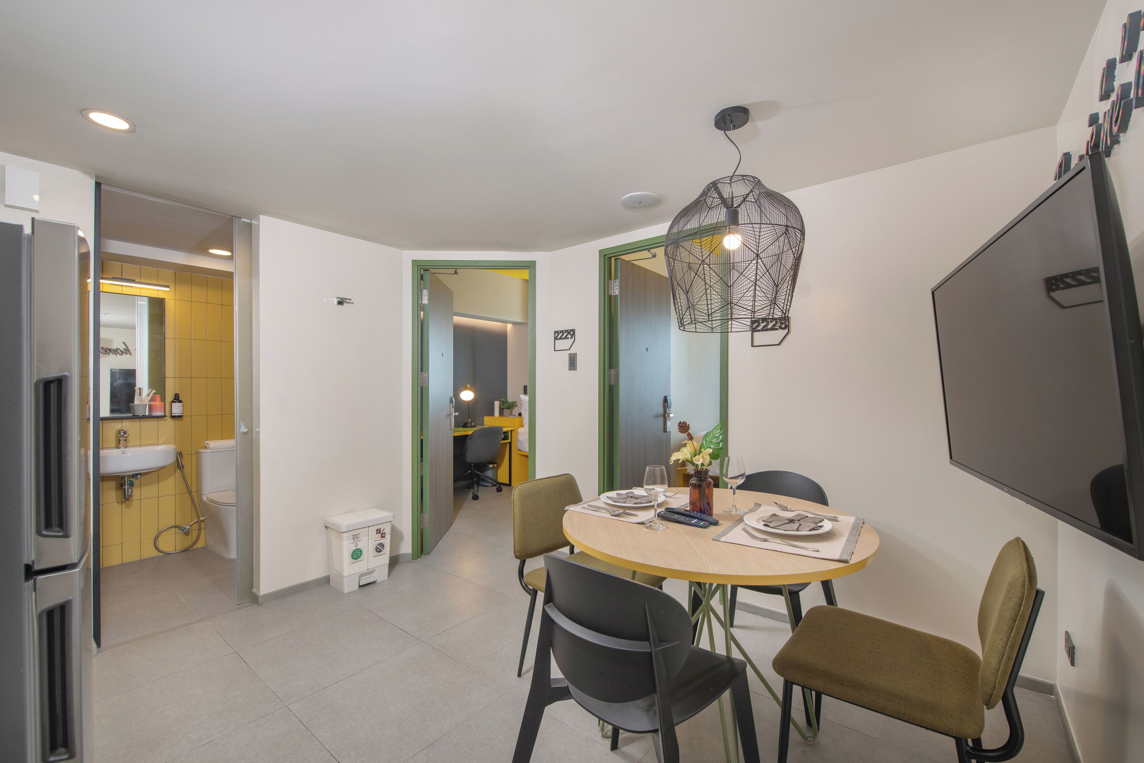 A modern kitchen with a dining area, a large flat-screen TV, and a unique pendant light.