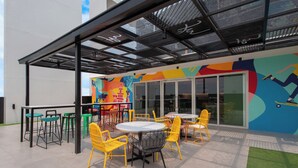An outdoor patio area with yellow and green chairs, a round table, and a colorful mural on the wall. - lyf Malate Manila managed by The Ascott Limited (Manila)
