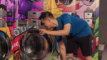 A person interacting with a wall-mounted laundry machine, a basket, and a colorful mural with a building illustration.