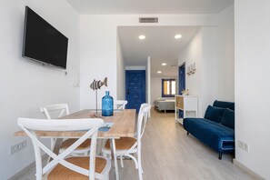 A modern living room with a dining area, a blue sofa, and a TV mounted on the wall.
